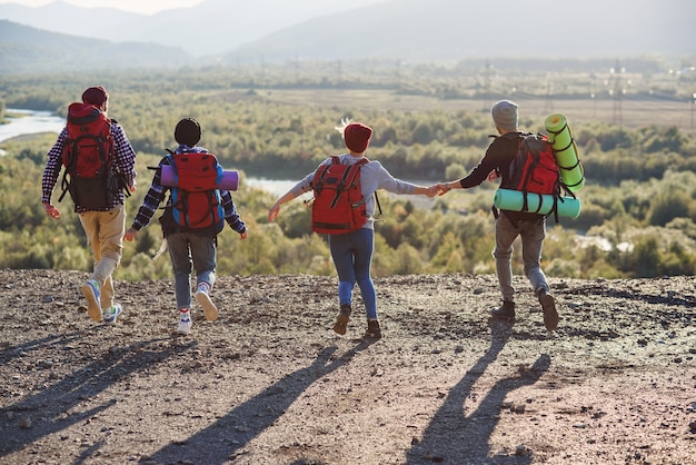 View from back of four hipster friends with travel backpack holding hands