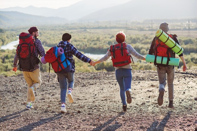 Vista dal retro di quattro amici hipster con zaino da viaggio per mano