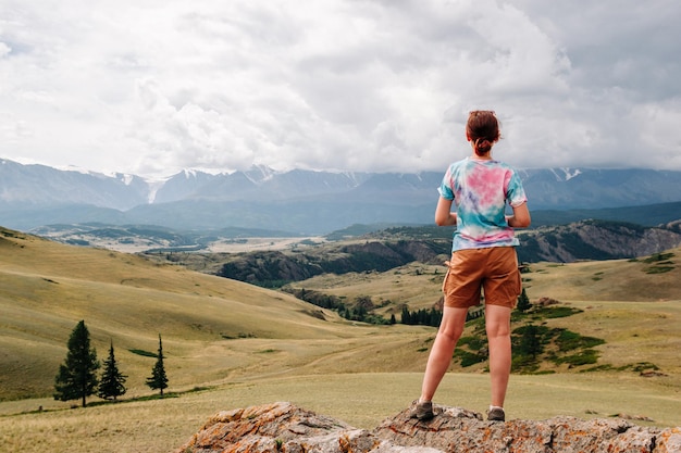 Вид со спины девушки, стоящей на краю обрыва на фоне красивой горной долины
