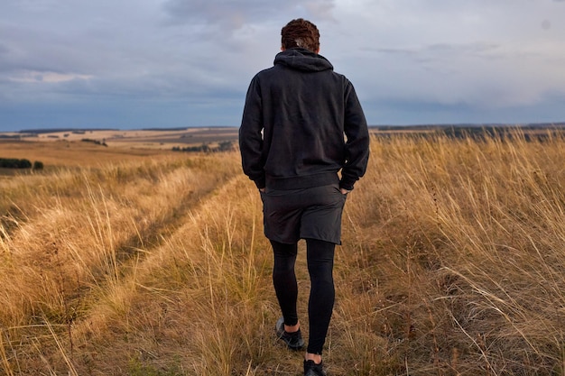 Вид сзади на человека, идущего в поле после пробежки, в спортивной одежде