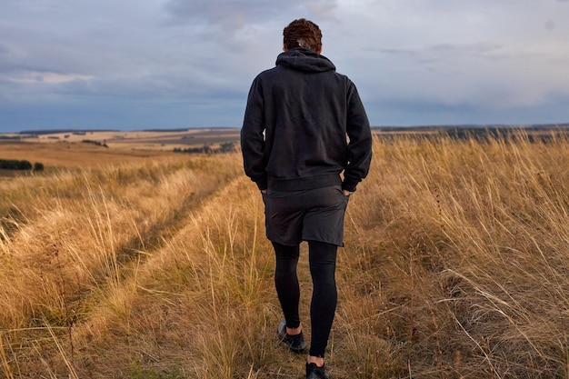 Vista da dietro dell'uomo che cammina nel campo dopo aver fatto jogging, in abiti sportivi