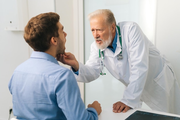 view from back to mature adult male doctor otolaryngologist performing examination of young man