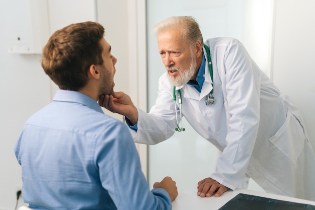 View from back to mature adult male doctor otolaryngologist performing examination of young man