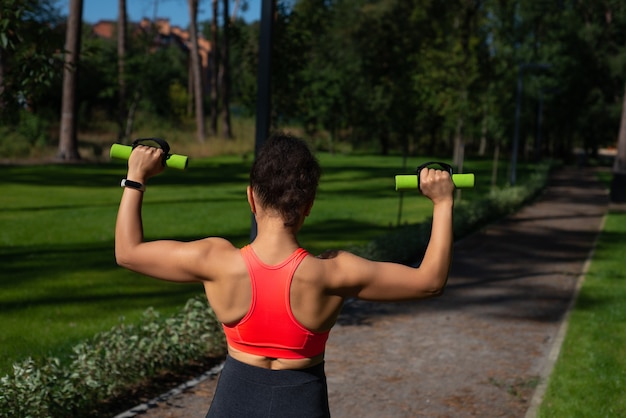 View from the back to woman pumping the muscles of the back and shoulders