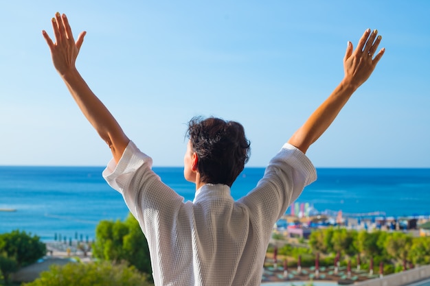 view from the back of a woman with open hands on balcony in summer morning.