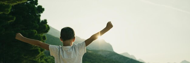 사진 떠오르는 태양에 의해 백라이트가 비추는 일출을 바라보며 삶을 축하하는 높이 들고 팔을 들고 서 있는 어린 소년의 뒤에서 보기 와이드 뷰 이미지