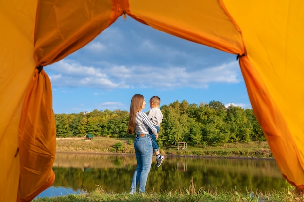 View from the camping tent. Girl enjoys nature holding child in her hands. Hiking with child