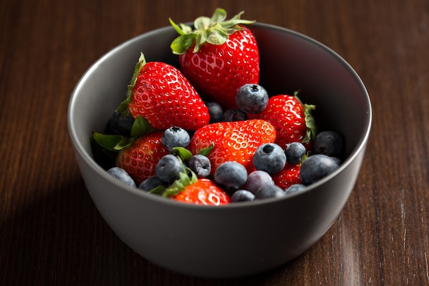 View from above closeup of fresh red berries, strawberries and blueberries in a bowl.