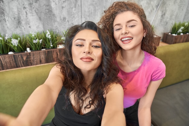 View from above of funny girls keeping phone in hands and doing selfie in cafe. 