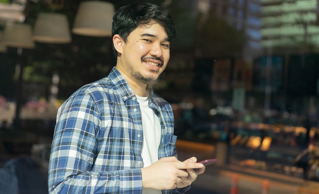 写真 中東の男のカフェのガラスからの眺め手持ちスマートフォンとコーヒーカフェで笑顔