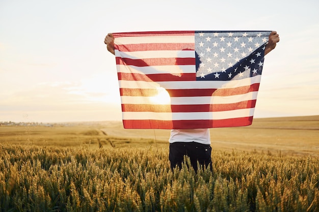 농업 분야에서 회색 머리와 수염을 가진 애국적인 수석 세련된 남자 손에 미국 국기를 들고 뒤에서보기