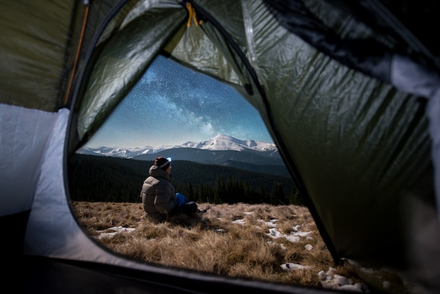 Вид изнутри палатки на мужчину-путешественника, отдыхающего в его кемпинге ночью