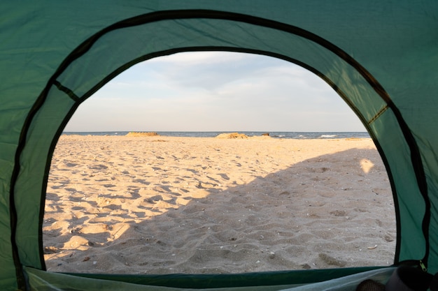 View from the Inside of tent at sea and sandy beach. Camping by the sea.