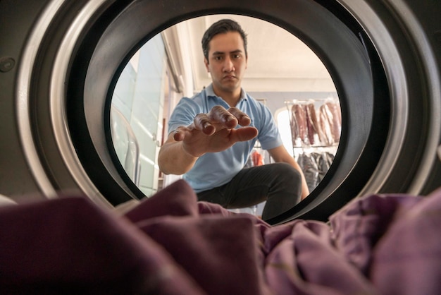 View from inside of the washer of a laundry worker male about\
to take out the laundry. young man working in laundry room.