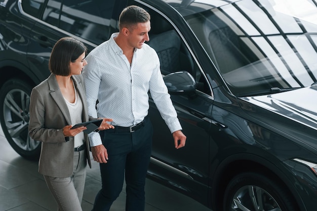 View from above Man in formal wear helping customer with choice of the automobile