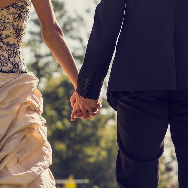 View from behind of newlywed couple, bride and groom,  holding hands outside on a sunny day, retro effect faded look.