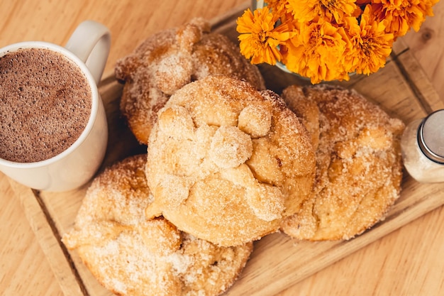 View from above of pan de muerto, a cup with chocolate and traditional Mexican flowers.