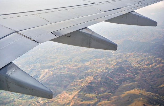 旅客機の乗客の窓からの眺め、航空機の翼の下に見えるぼやけた山岳地帯のアフリカの風景