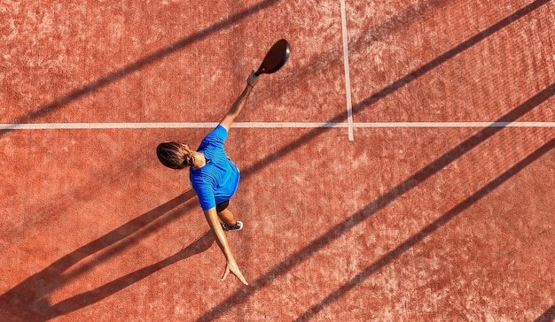 View from above of a professional paddle tennis player who has just hit the ball with his racket on an outdoor court.