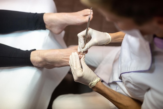 View from above of professional pedicurist removing cuticle with steel tool while making pedicure