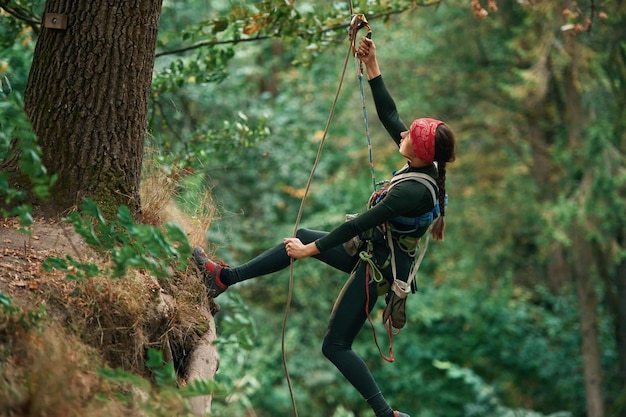 Foto vista dal lato appesa alla corda la donna sta facendo arrampicata nella foresta con l'uso di attrezzature di sicurezza