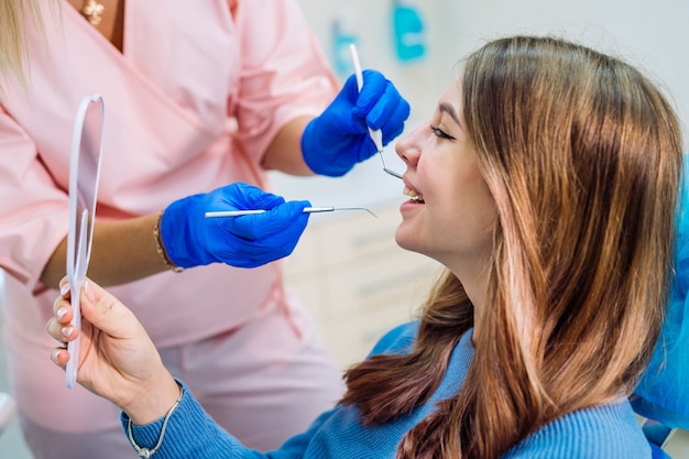 Вид со стороны счастливой пациентки, смотрящей в зеркало и наслаждающейся красивой улыбкой в стоматологическом кабинете