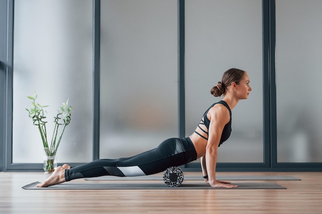 Вид со стороны Молодая женщина в спортивной одежде и со стройным телом проводит день фитнес-йоги в помещении