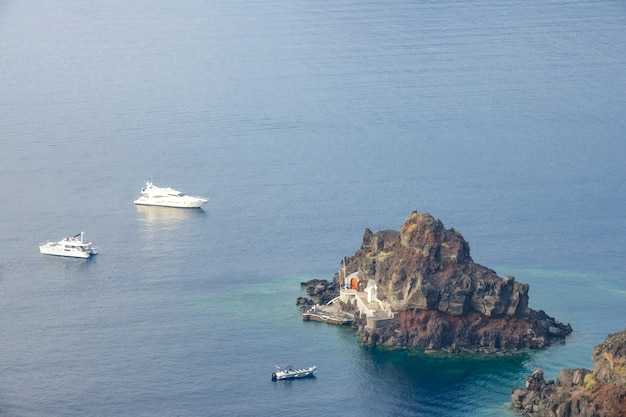 View from above on a small rocky island with a pier. Two yachts and a pleasure motor boat anchored nearby