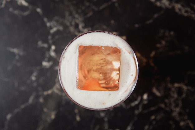 A view from above of a sour cocktail with a big ice cube on black marble table