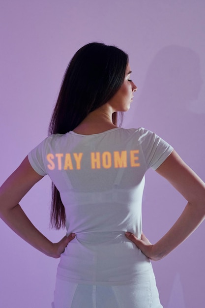 View from behind stay home words beautiful young woman is in\
projector neon lights in the studio