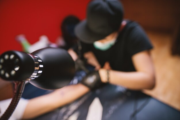 View from above of tattoo artist inking customers arm in his shop.