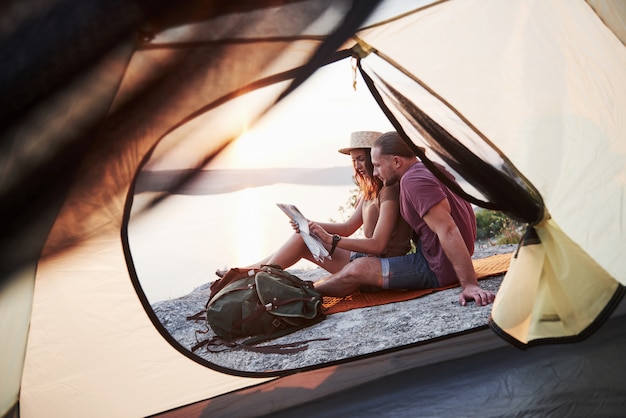 ハイキング旅行中に湖の景色を横になっている地図が付いているカップルのテントからの眺め。 avelライフスタイルコンセプトアドベンチャーバケーションアウトドア
