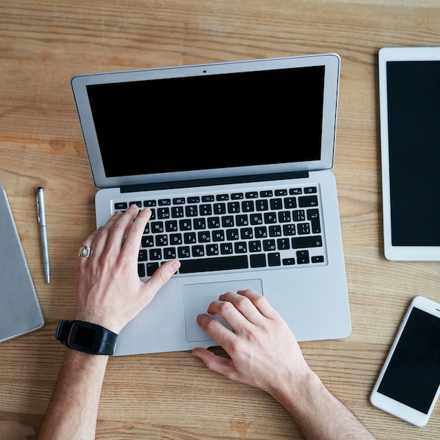 Vista dalle mani superiori che lavorano con laptop e smartphone su un tavolo di legno