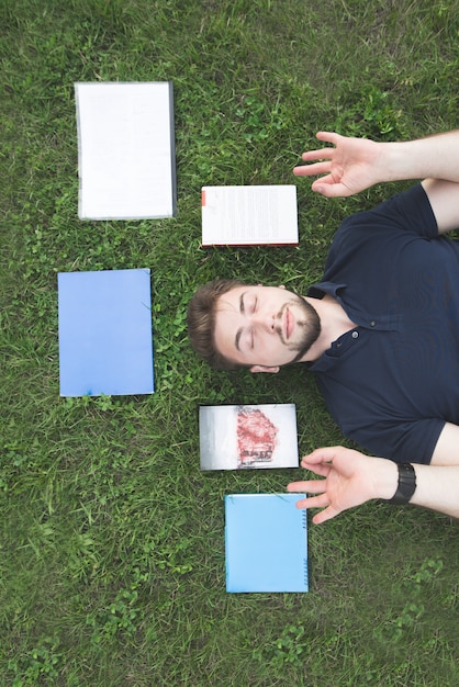 View from the top of a handsome man lying on the grass with books and meditating.