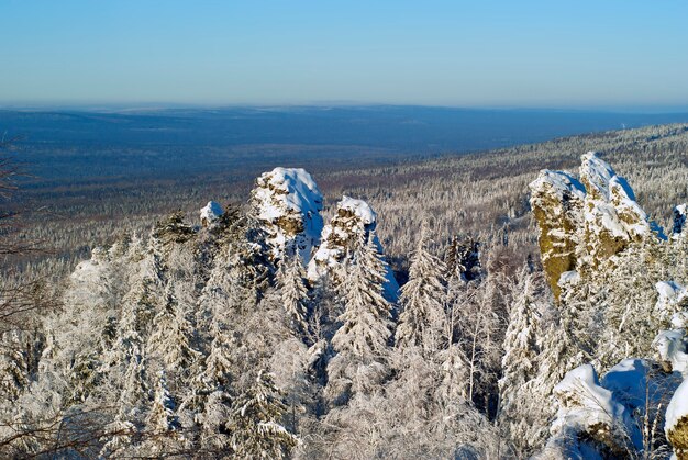 View from the top of the Ural ridge on a winter day on wooded hills and rocks in the foreground