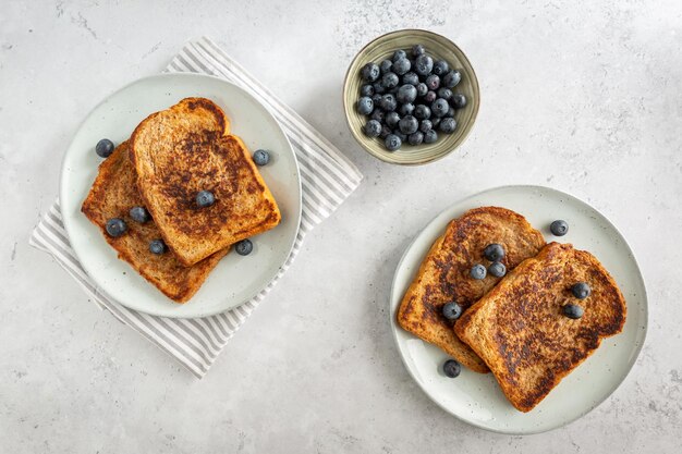 View from above of two plates with french toast with blueberries and a bowl of blueberries on a grey background from above minimalistic style with copy space