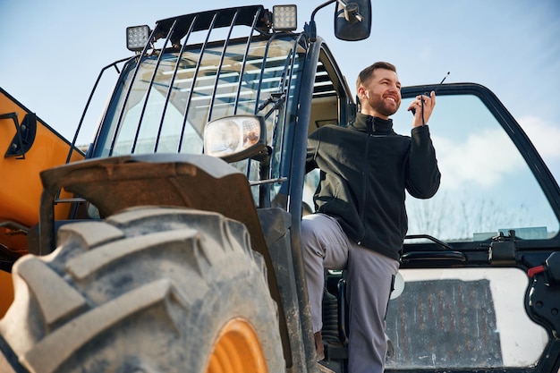 Photo view from below using walkie talkie man is with tractor agricultural worker