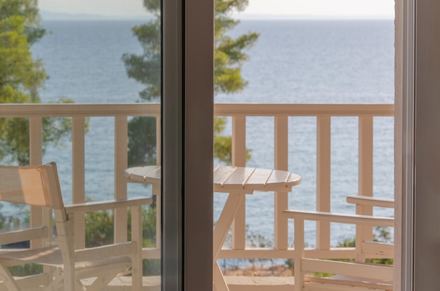 View from window to loggia with table and chairs and to sea Window frame in foreground creamcoloured garden set