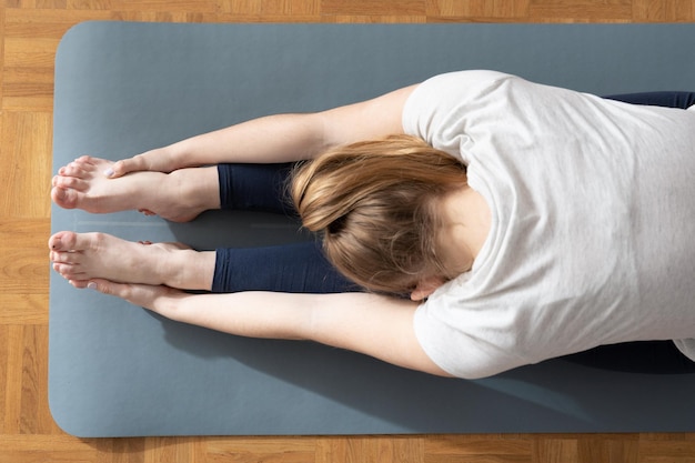 View from above of woman stretching hamstring muscles holding her feet with hands