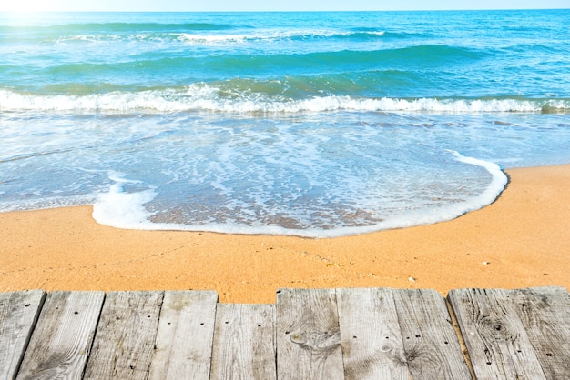 View from wooden desk on summer tropical beach with sand and sea wave at background