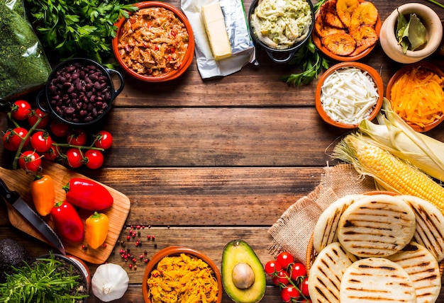 Vista dall'alto di un tavolo rustico in legno con diversi ingredienti per cucinare e riempire le arepas