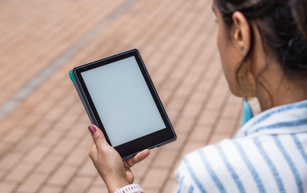 都市のシーンでタブレットを保持している若い女性の後ろからの眺め