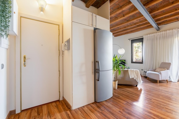 View of the front door from the inside in bright spacious living room combined with kitchen with modern decor elements and accessories and wooden beams on the ceiling European style concept