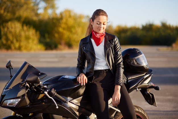View of good looking young woman dressed in black jacket, has stylish red bandana on neck