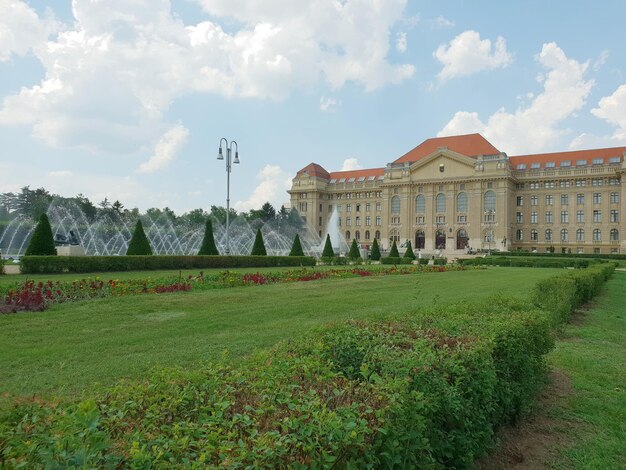 View of grassy field by historic building against cloudy sky