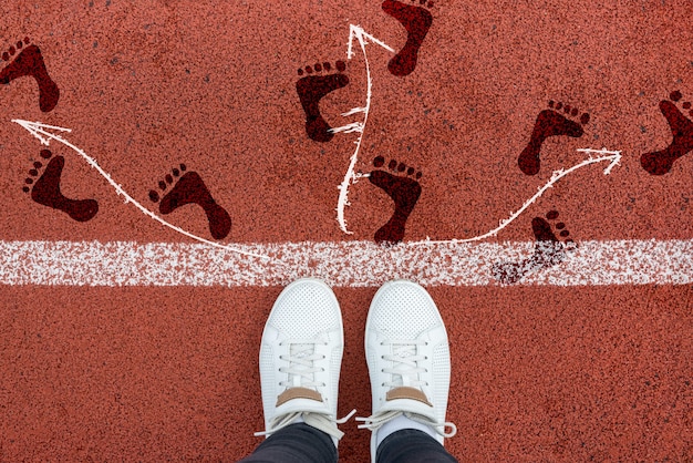 View of gray feet and arrows pointing in different directions\
on a red treadmill. decision making and choice. find your own path.\
direction of movement, intersection