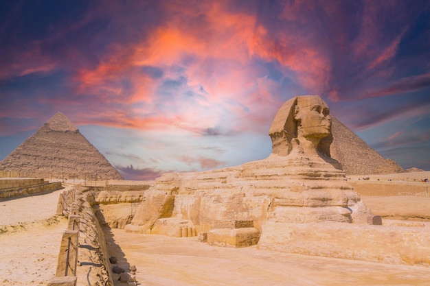 A view of the the Great Sphinx and the Pyramids of Giza against a colorful sunset at Giza, Egypt