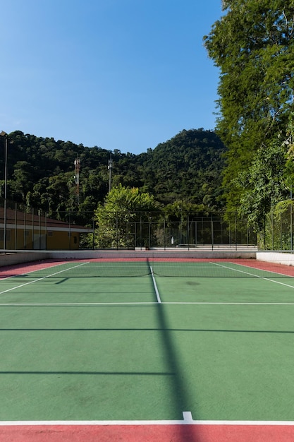Вид на зелено-красный теннисный корт с природой вокруг Широко используется для занятий спортом и игры в теннис