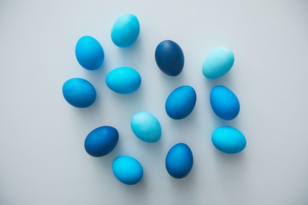 Above view of hand-painted blue Easter eggs arranged in minimal composition on white surface, copy space