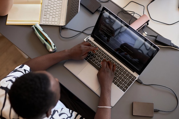 Above view of hands of African American male student typing on laptop keyboard while sitting by desk at informatics lesson and decoding data